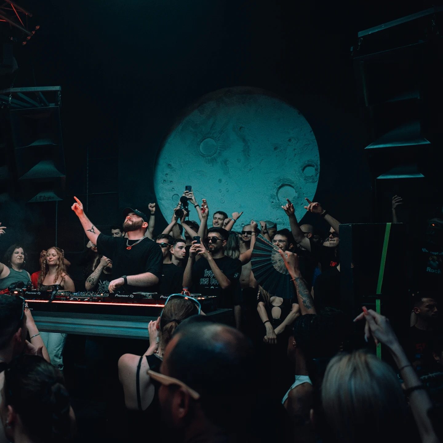 DJ na cabine do Moon Club com a Lua gigante iluminada atrás